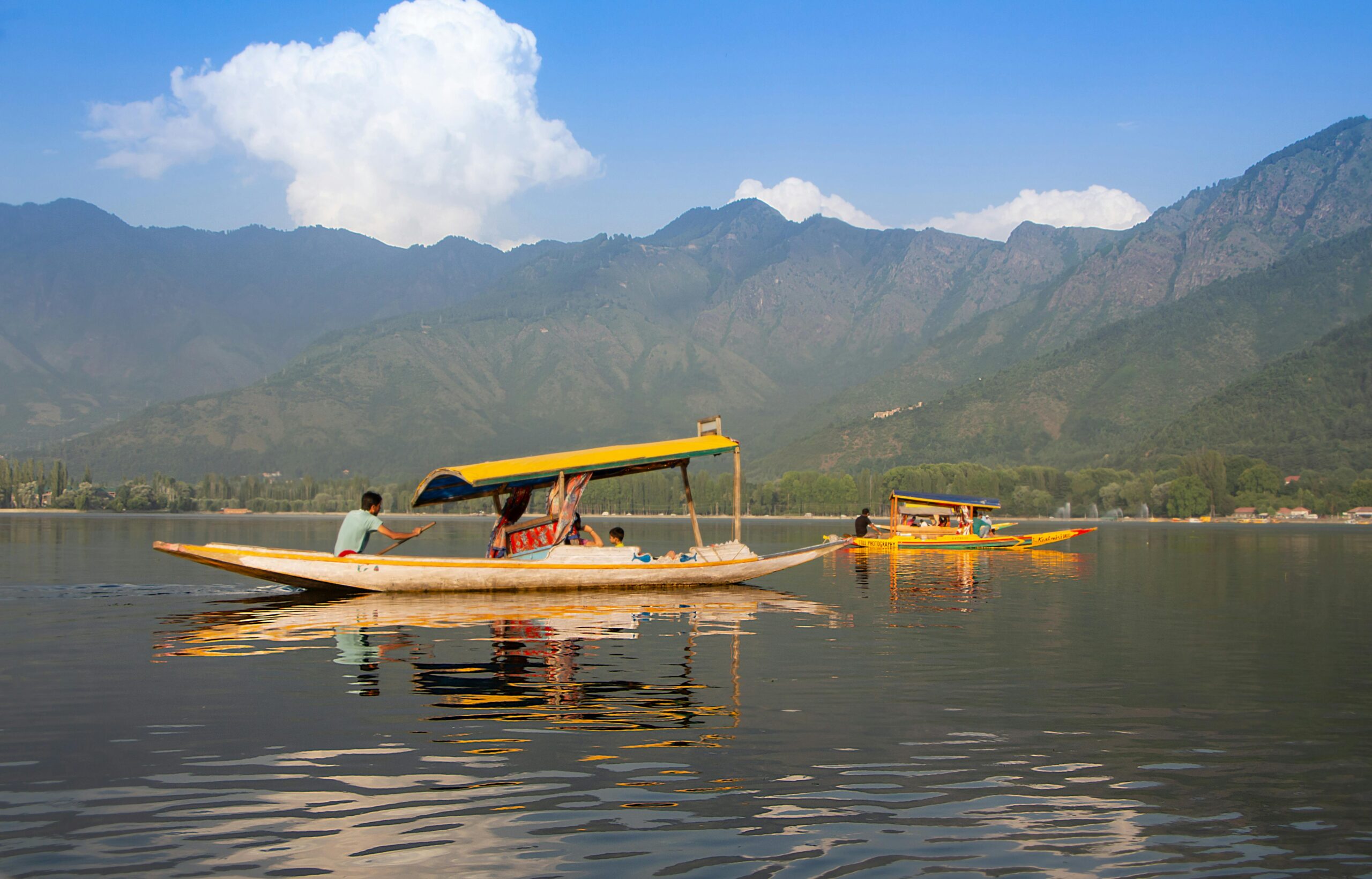 Shikara boats glide on a serene lake with majestic mountains in the background.